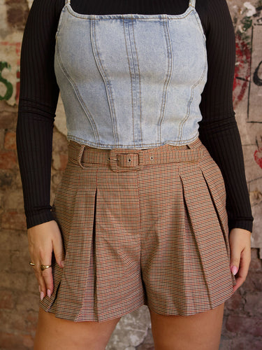 Model wearing mid-rise belted plaid shorts with pleated detailing in an unlined fabric with minimal stretch.