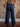 Model wearing mid-rise wide-leg jeans with exposed side seams, a button and zipper closure, and classic 5-pocket design with stretch.