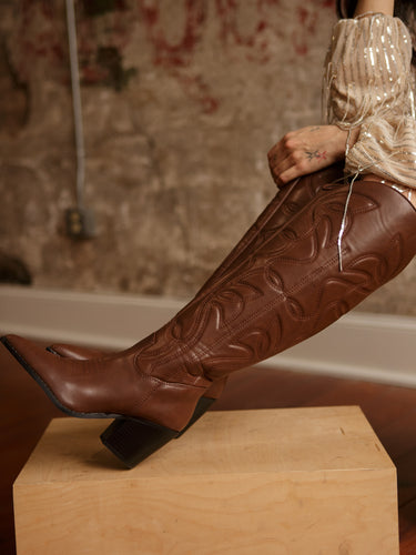 Knee-high faux leather western-inspired boots with embossed stitching, inner zipper, cushioned footbed, and 2.5-inch block heel.
