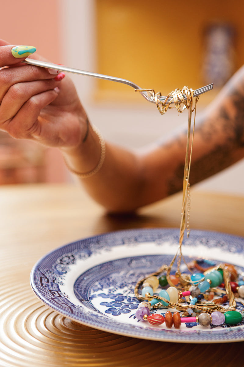 A plate full of beaded necklaces and a gold chain on a fork