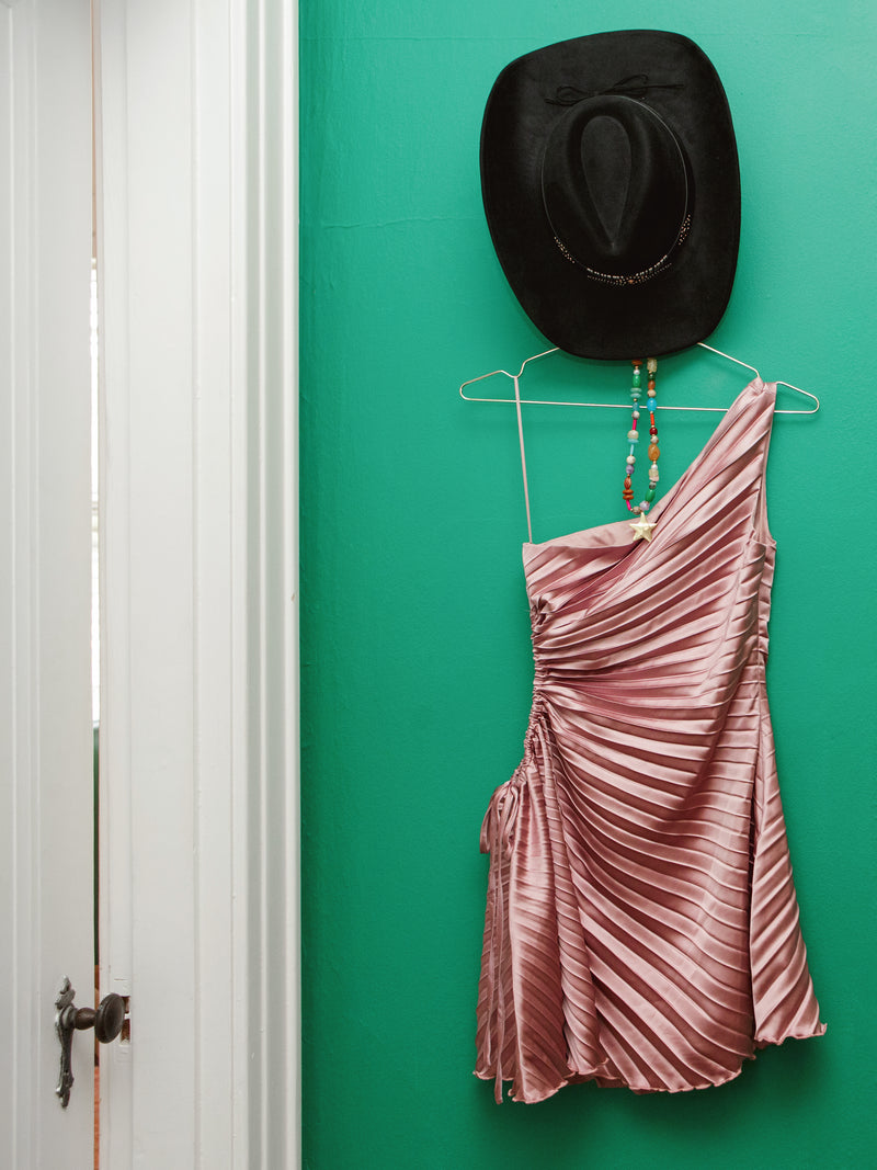Chelley One shoulder dress with a black hat on a green wall