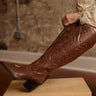 Knee-high faux leather western-inspired boots with embossed stitching, inner zipper, cushioned footbed, and 2.5-inch block heel.