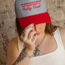 Trucker-style hat with red brim, embroidered front, and plastic adjustable snap closure.