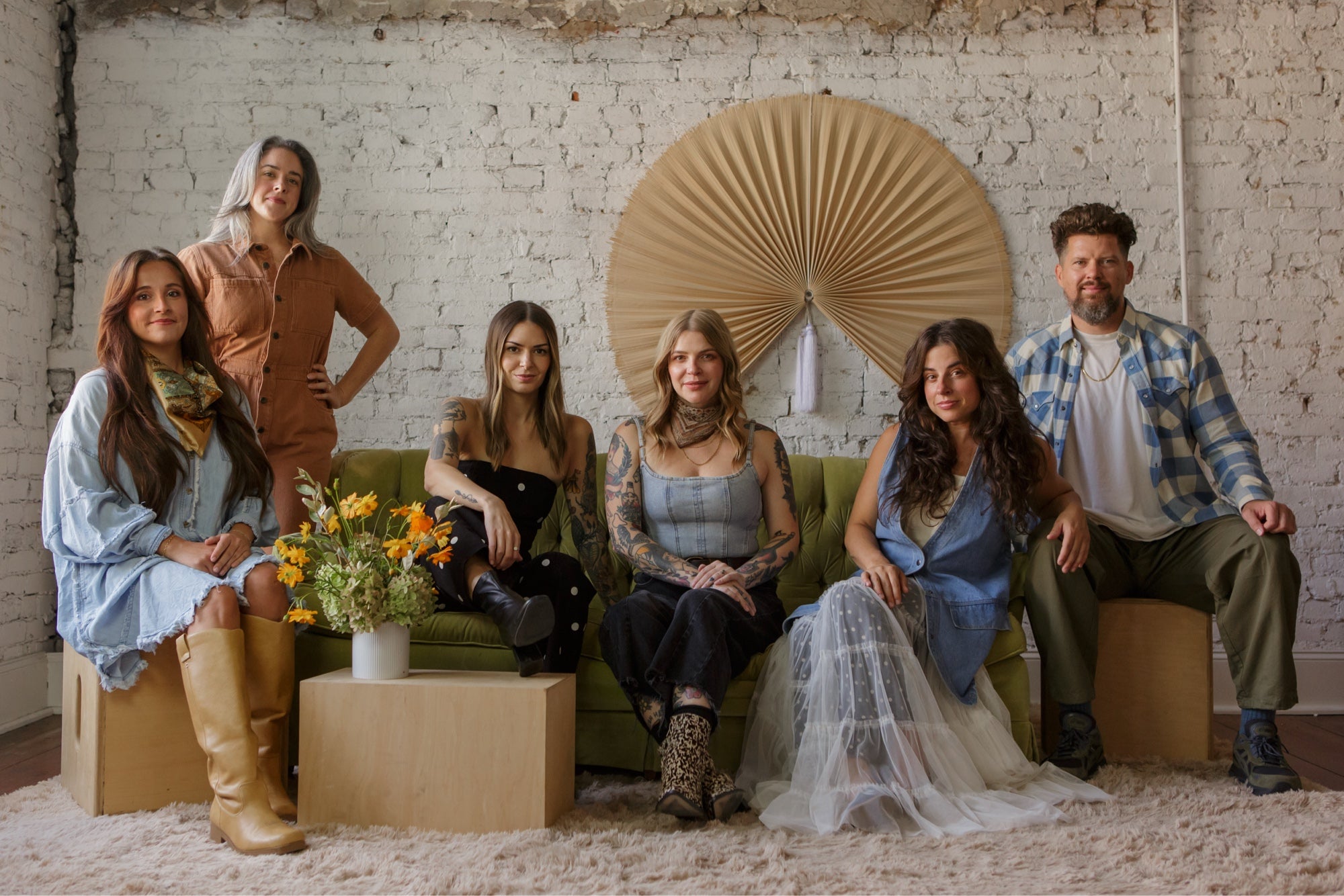 The Molly Green team gathered on the green velvet couch in front of a woven fan backdrop
