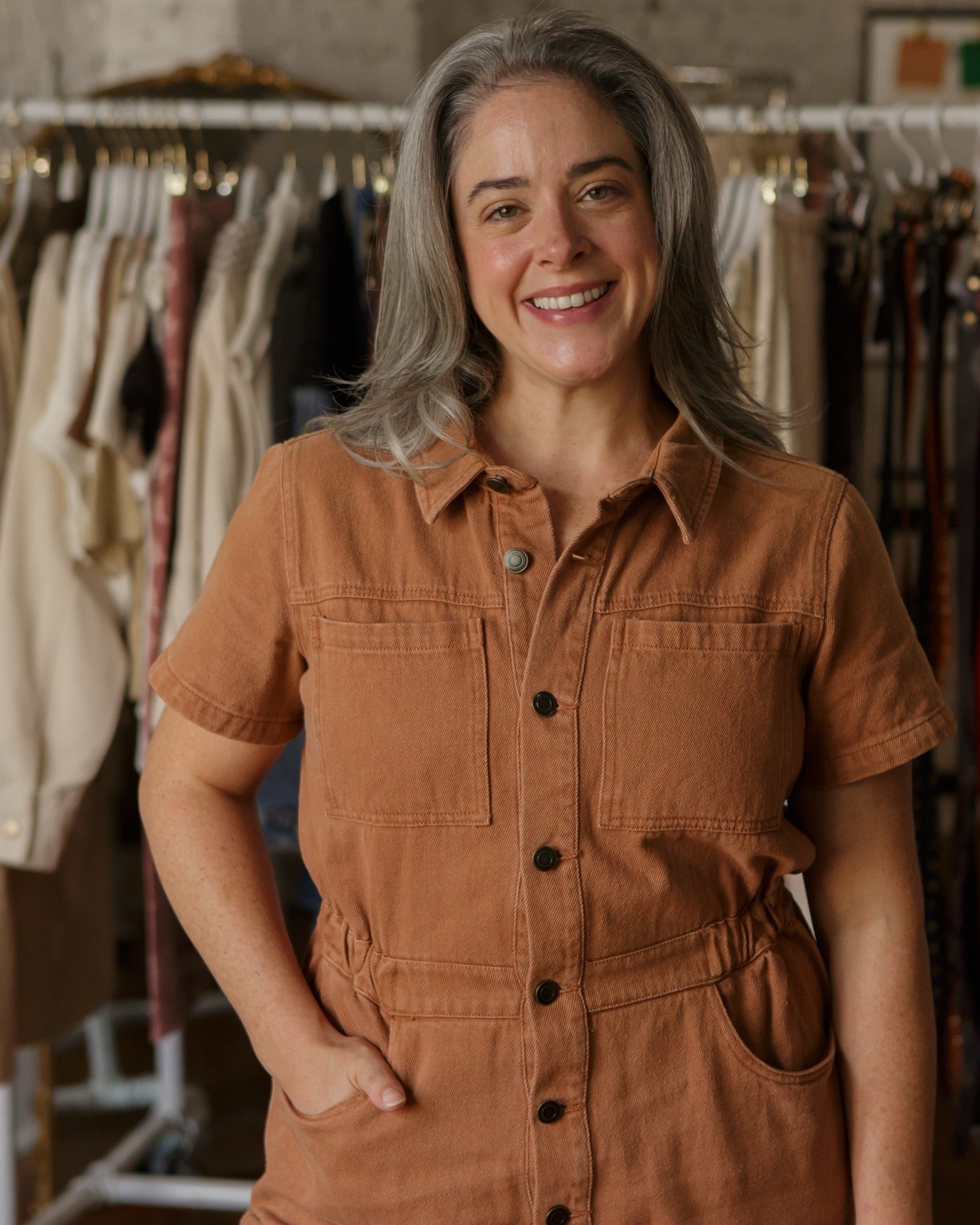 Anna Spainhour smiling in a rust utility jumper in front of a clothing rack
