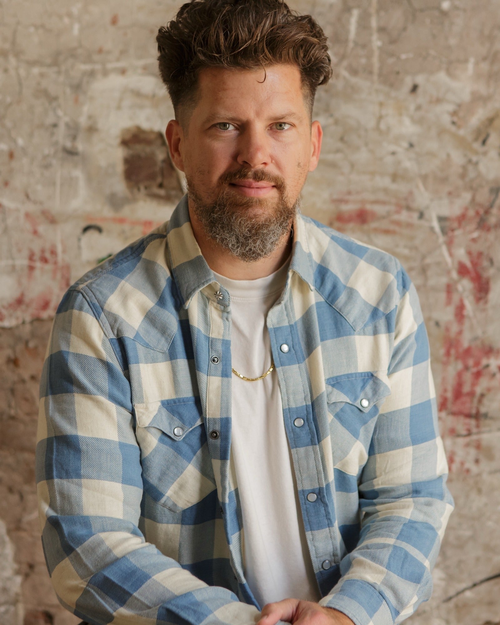 Brandon Hartwell in a blue and cream plaid shirt against a distressed brick wall
