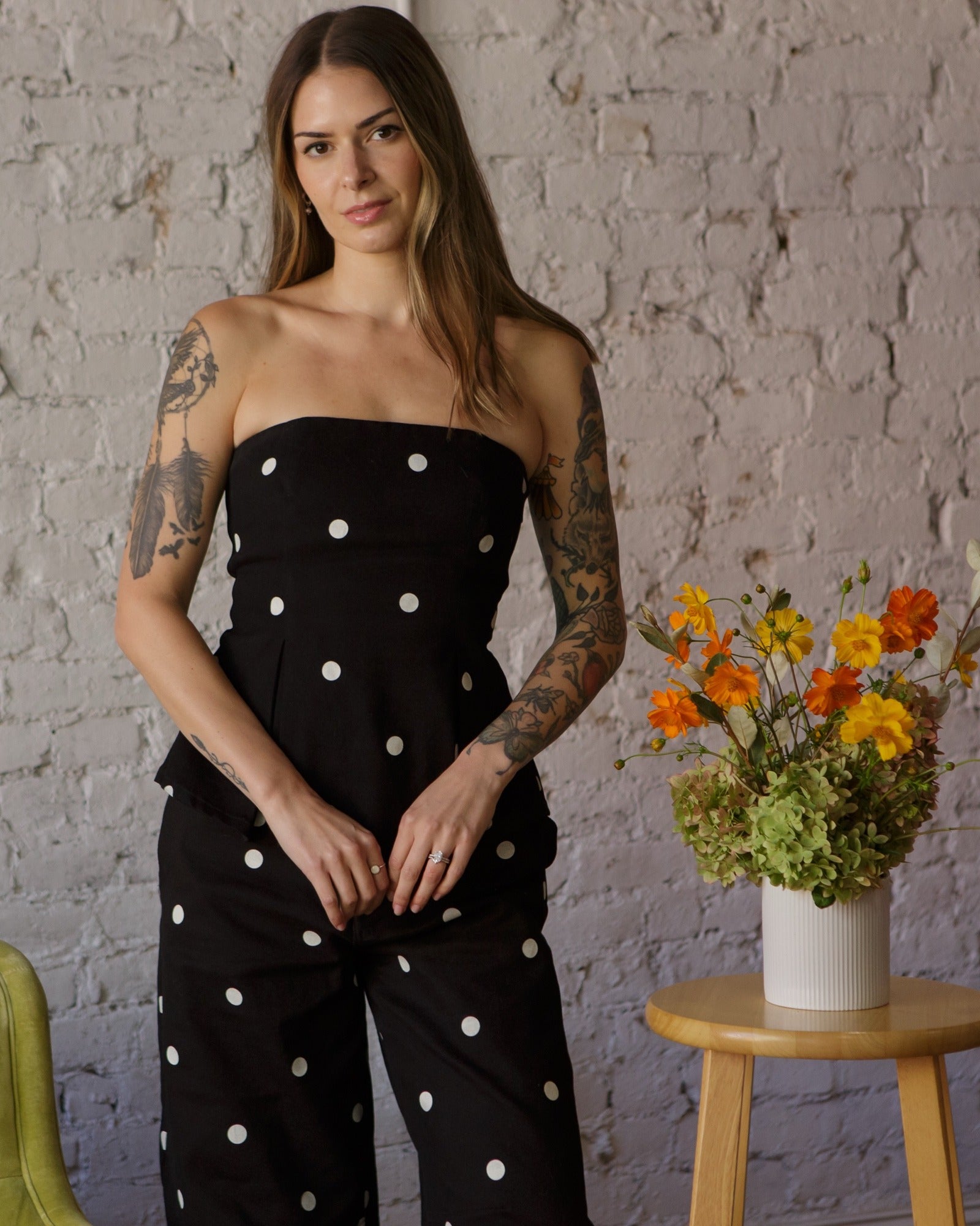 Kelsey DeMarco in a black polka dot matching set beside a vase of orange cosmos