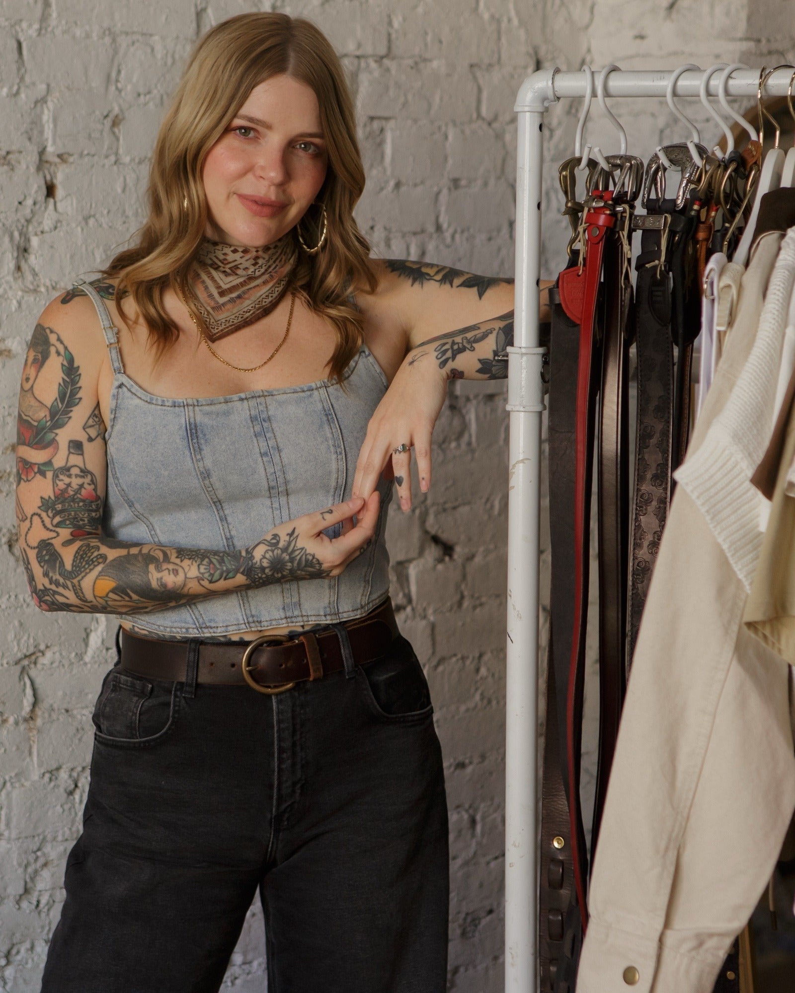 Heather Johns in a denim corset top and black jeans standing beside a rack of belts