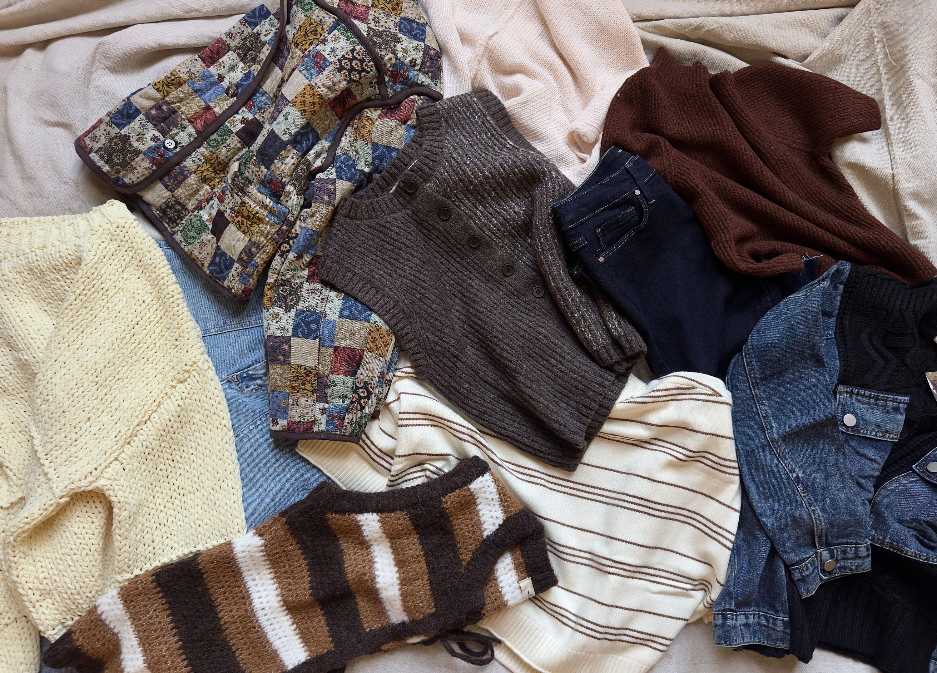 A layered fall outfit on light bleached oak — cream cable knit, denim, caramel boots, camel coat
